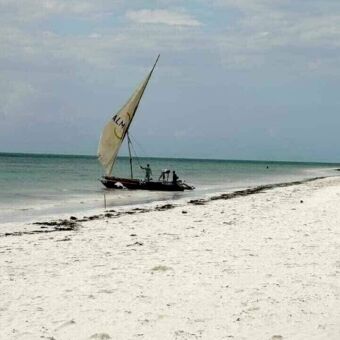 Wit strand met aan de kant een dhow zeilboot met daarin de vissers