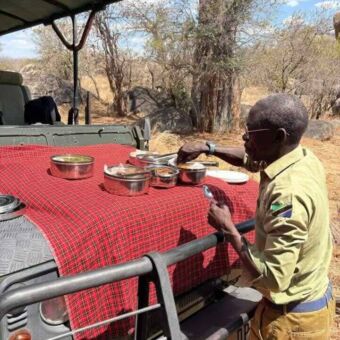 Op de motorkap van de safari auto ligt een kleedje met daarop de lunch die wordt neergezet door de gids