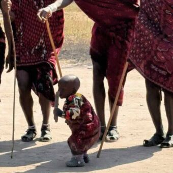 Masai peuter die ook meespring en danst met de andere drie masai's