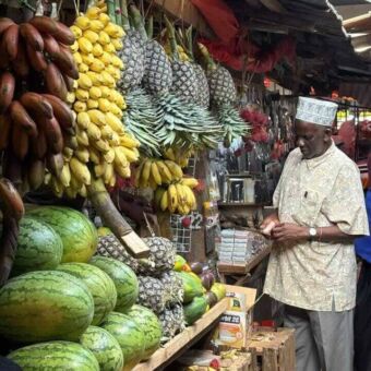 Groentestal met alerlei groenten en fruit en de verkoper die erbij staat