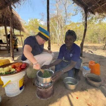 Vrouw op vakantie die samen meteen lokale vrouw eten maakt en in een pan roert