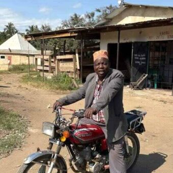 Man op een brommer voor een huis erop een zandweg in Zanzibar