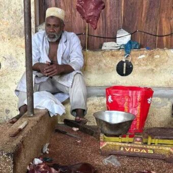 Man gekleed in het wit zit bij zijn eenvoudige marktkraam waar hij vlees verkoopt