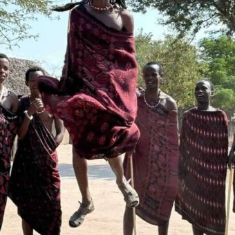 vier masai mannen waarvan de middelste in de lucht spring met een stok in zijn hand