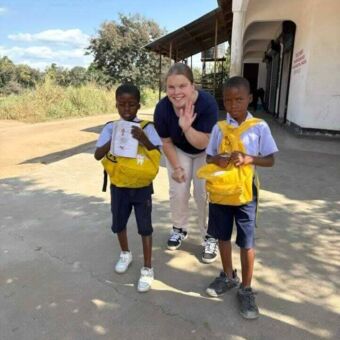 twee kindjes in schooluniform met daar tussen in een vrouw die zwaait