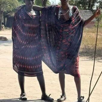Twee masai mannen in kleurige kleden met stokken die naast elkaar staan en met de arm om de ander