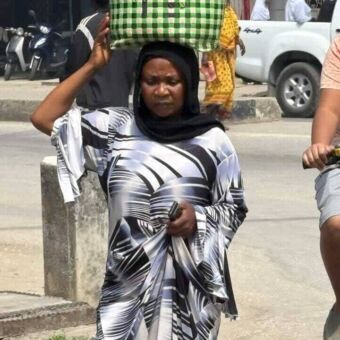 In zwart wit geklede vrouw loopt met een groen mand op haar hoofd door de straten van Stone Town