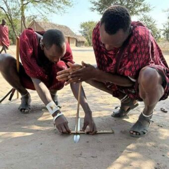 Twee masai mannen die vuur aan het maken zijn met een stokje op een zwaard