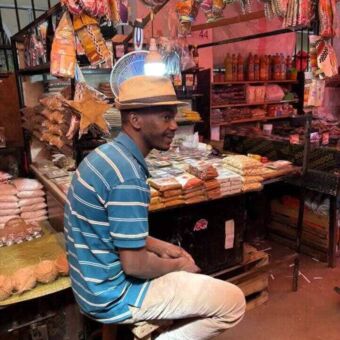 Man met hoedje die bij zijn kraam met kruiden zit en lacht