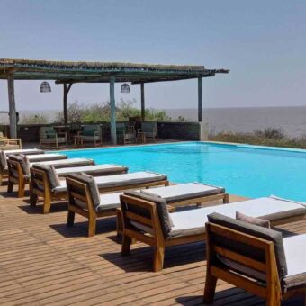 logstoelen bij een zwembad met daarachter Lake Manyara