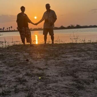 man en vrouw houden elkaars handen vast bij een zonsondergang aan het water