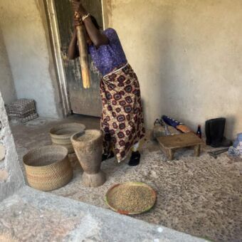 Vrouw met een grote houten paal stamt de mais in een pot fijn